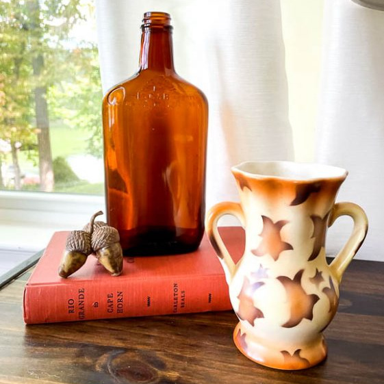 Fall vignette with a Czech vase, amber bottle, acorns and an orange book