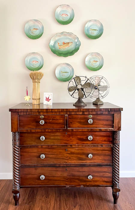 Antique fish platter hanging over a dresser decorate with vintage fans and a fall vignette