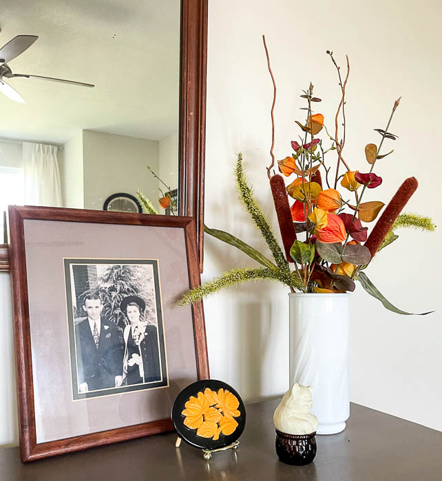 Fall floral arrangement, 1930s wedding picture and belt buckle, Avon cat with basket