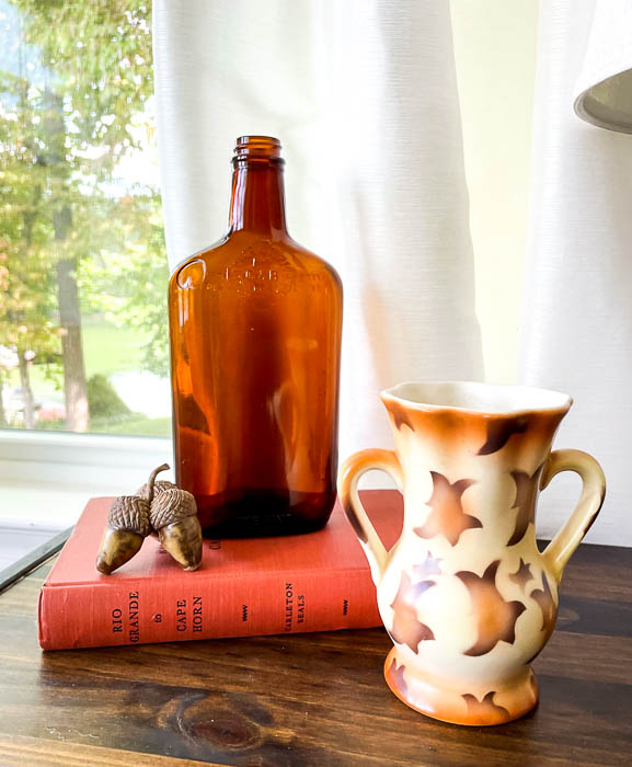 Fall vignette with a Czech vase, amber bottle, acorns and an orange book