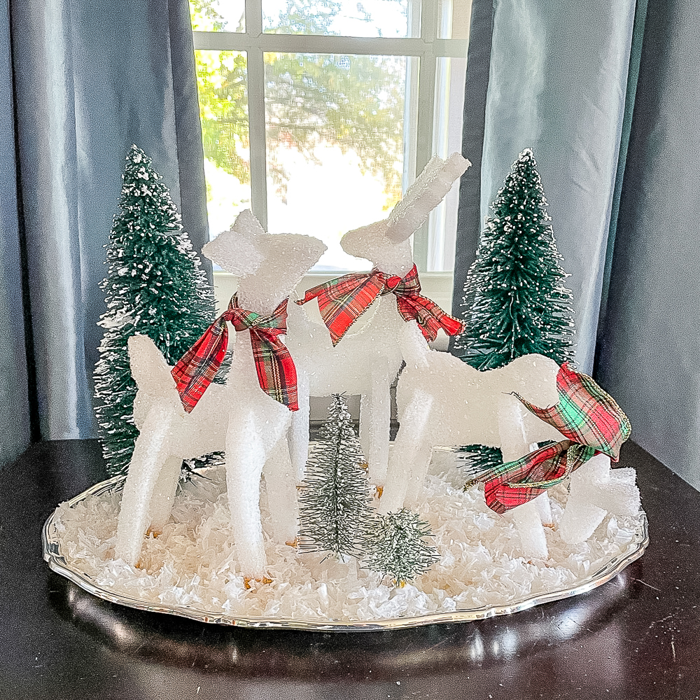Reindeer crafted from Styrofoam with plaid scarves on a silver tray with snow and trees