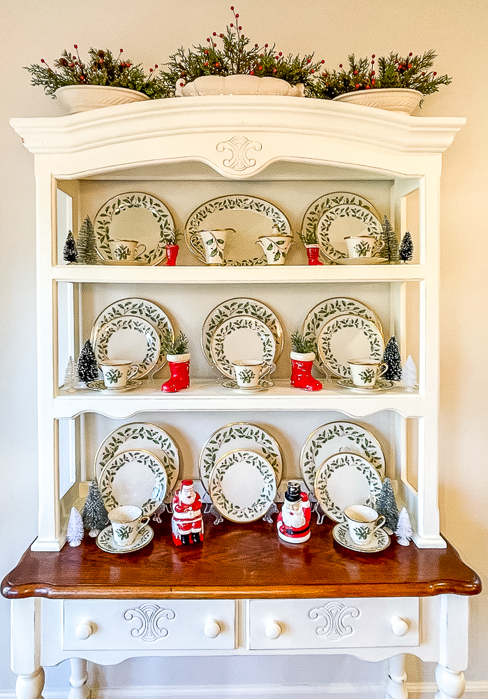 Hutch decorated for Christmas with Lenox Holiday dishes, vintage Santa boots, vintage Santas and bottlebrush trees