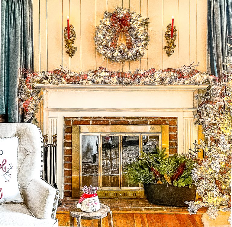 Fireplace decorated for Christmas with a flocked wreath and garland, red plaid ribbon, red berries, and red candles