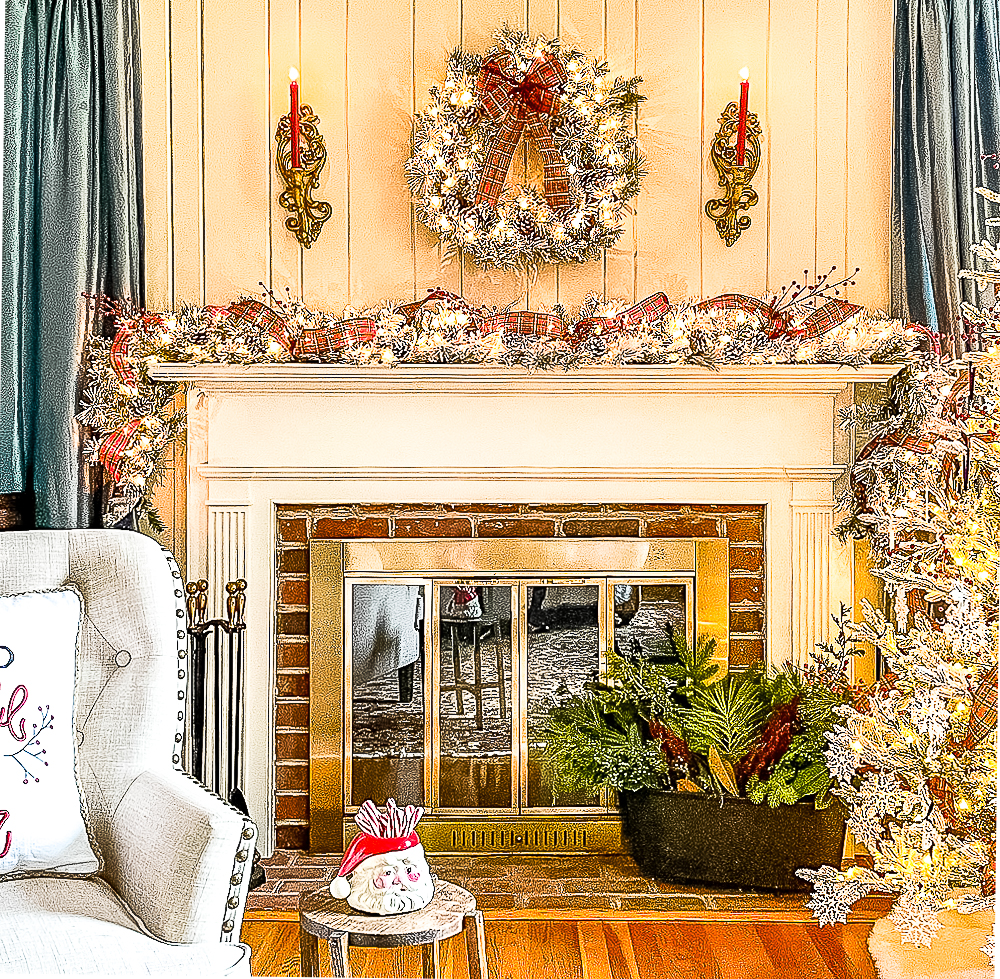 Fireplace decorated for Christmas with a flocked wreath and garland, red plaid ribbon, red berries, and red candles